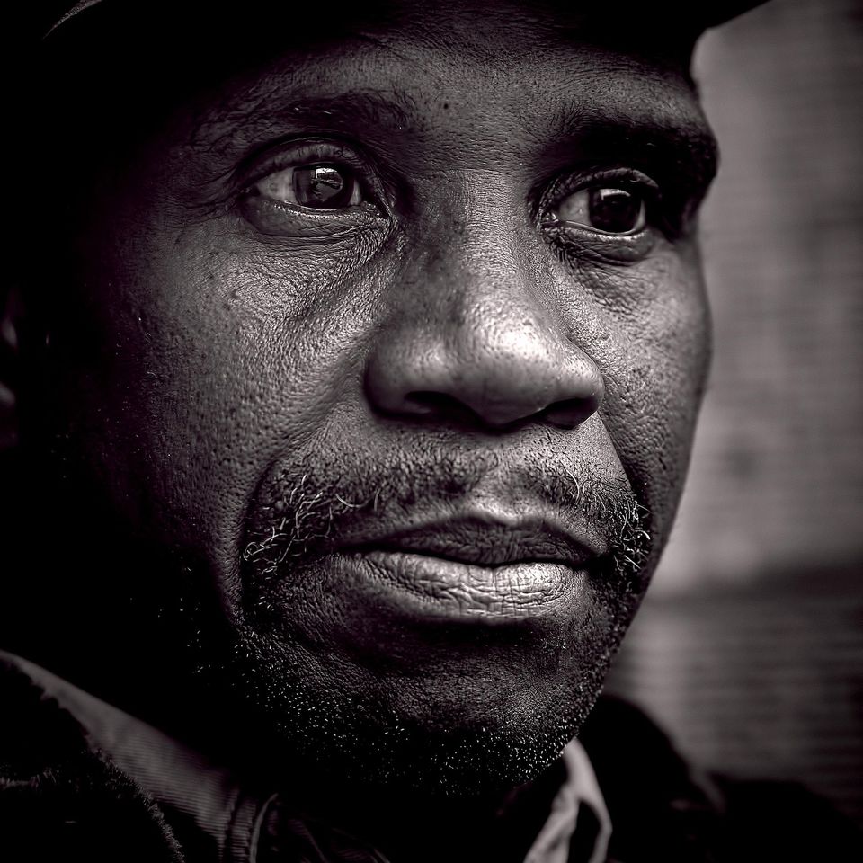 “Close-up black-and-white portrait of a man looking thoughtful, representing resilience and dignity in the face of hardship.”