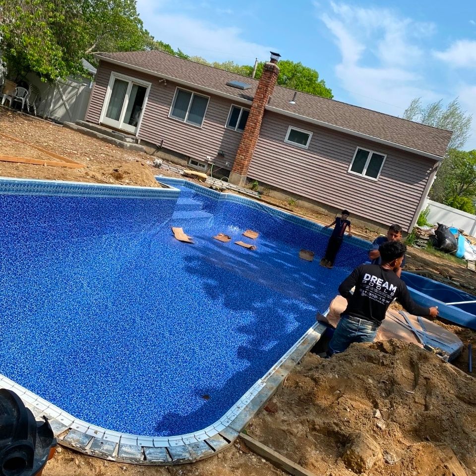 Crew installing a vinyl pool liner in a freeform inground pool behind a Long Island home