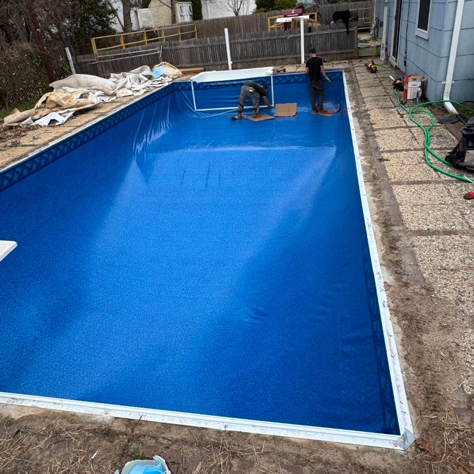 Two technicians smoothing a new blue liner across a rectangular inground pool in Long Island NY