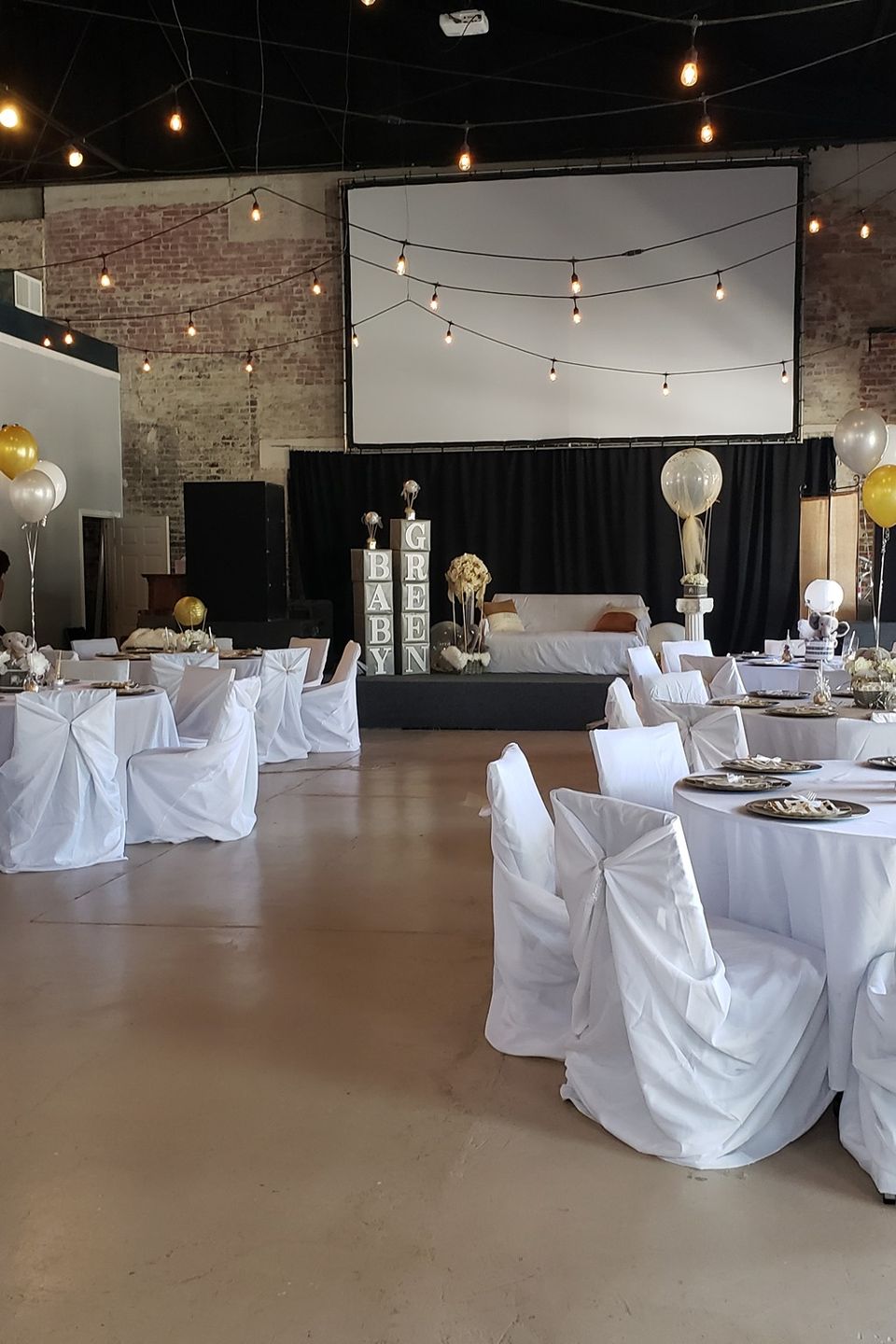 Indoor event venue decorated with elegant white table settings, balloons, and stage display for a Carpe Diem Events celebration