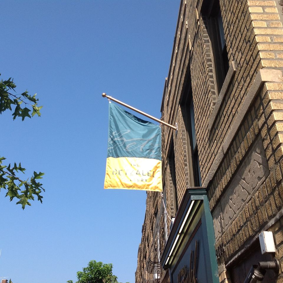 Two-tone teal and yellow fabric flag sign on a pole bracket projecting from a brick facade
