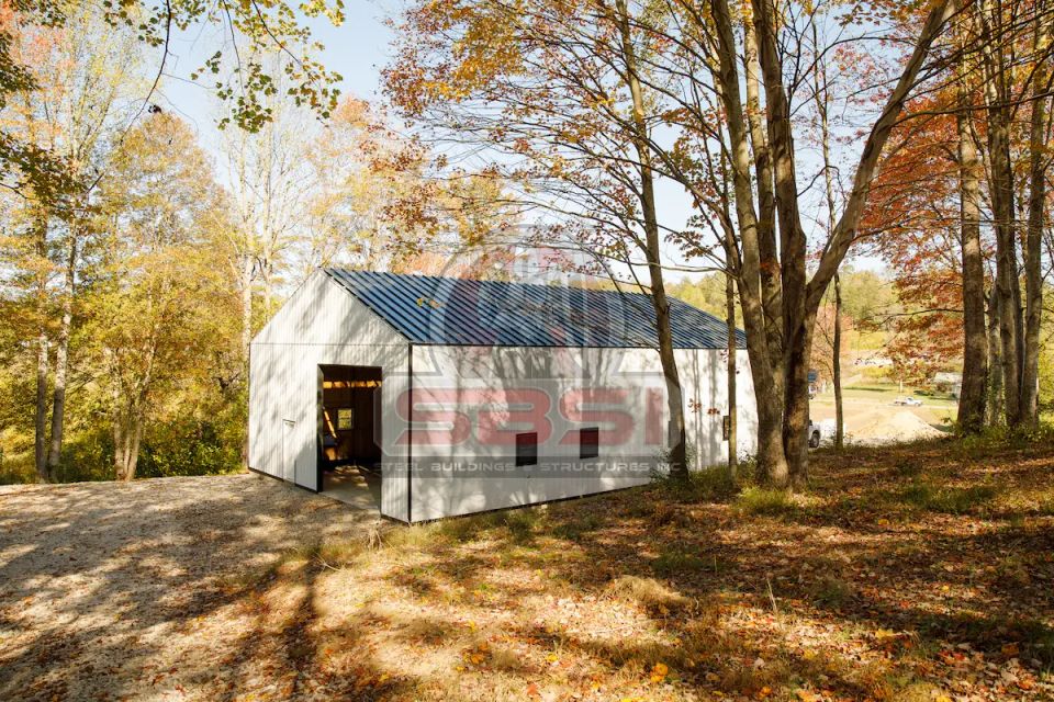 White steel building with blue roof and open door in autumn wooded lot with SBSI watermark representing steel buildings in Alabama