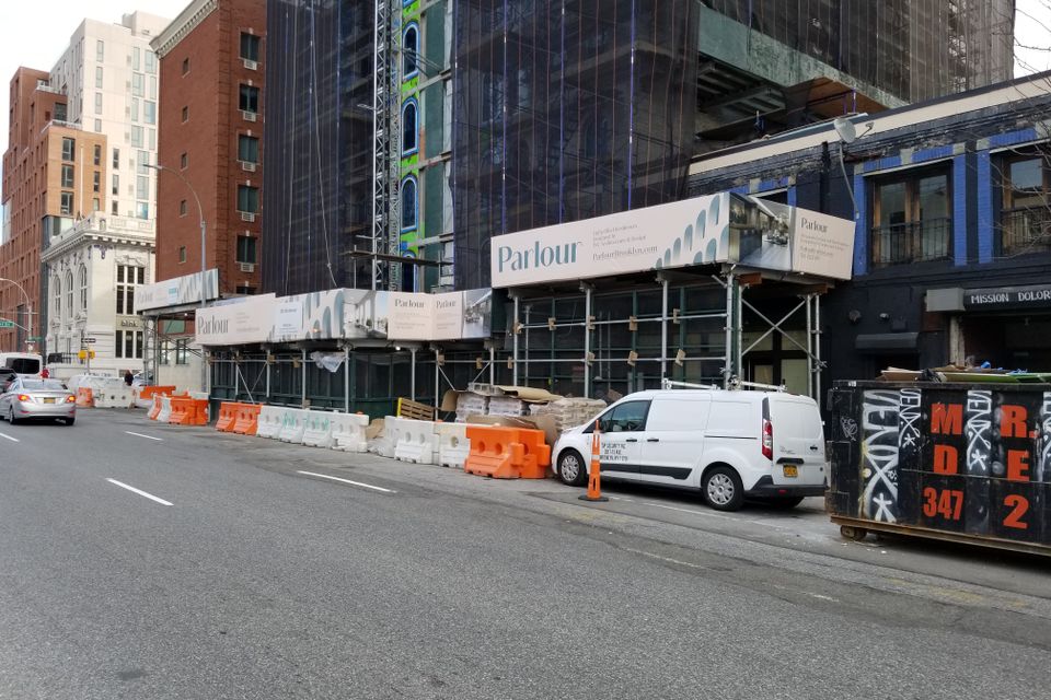 Printed banner panels wrapping a sidewalk shed on a Brooklyn corner
