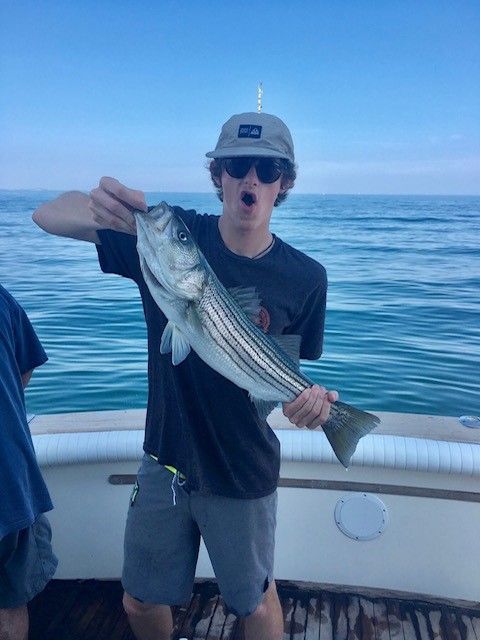 Young man back of boat hat sunglasses holding striped bass