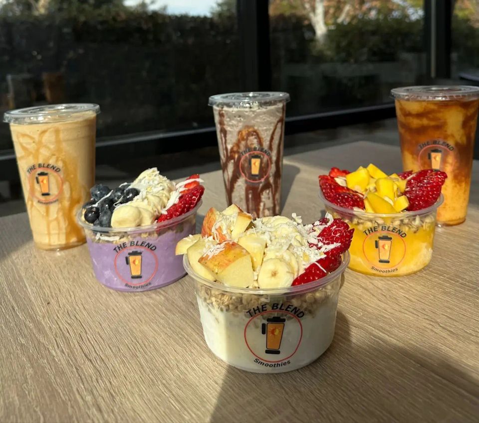 A creamy smoothie in a clear plastic cup, drizzled with caramel or peanut butter.
A purple acai bowl topped with bananas, blueberries, and strawberries, garnished with shredded coconut and granola.
A white yogurt or smoothie bowl topped with apples, strawberries, granola, and coconut flakes.
A yellow/orange bowl with mango chunks, strawberries, and granola in a tropical base.
A chocolate shake or smoothie with a drizzle on the inside of the cup.
An amber iced tea or juice beverage in a clear cup.