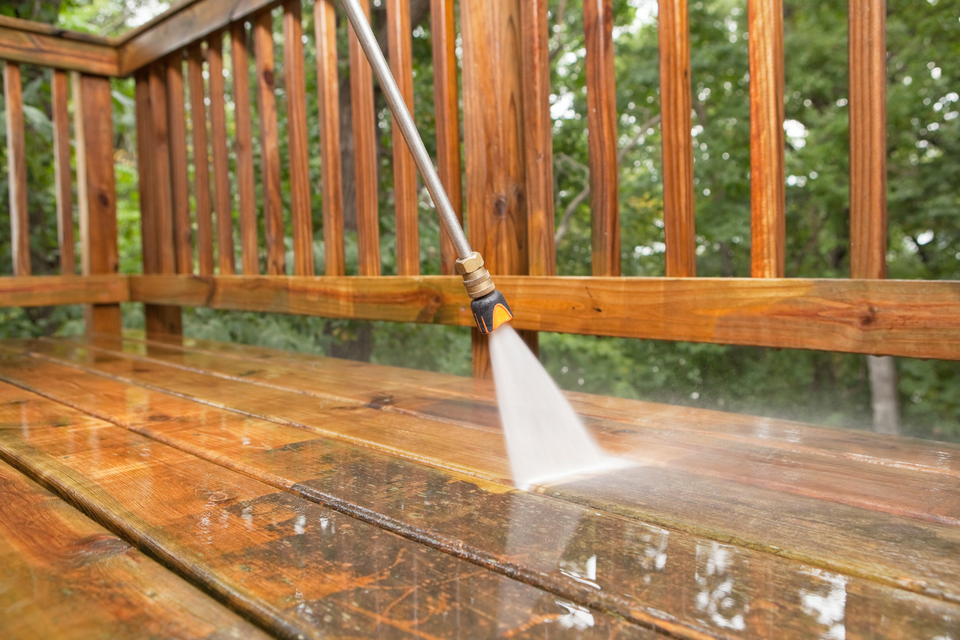 Pressure washing a wooden deck to remove dirt, algae, and weather-related buildup from the surface.