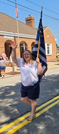 Woman waving while carrying an American flag during a Fourth of July parade.