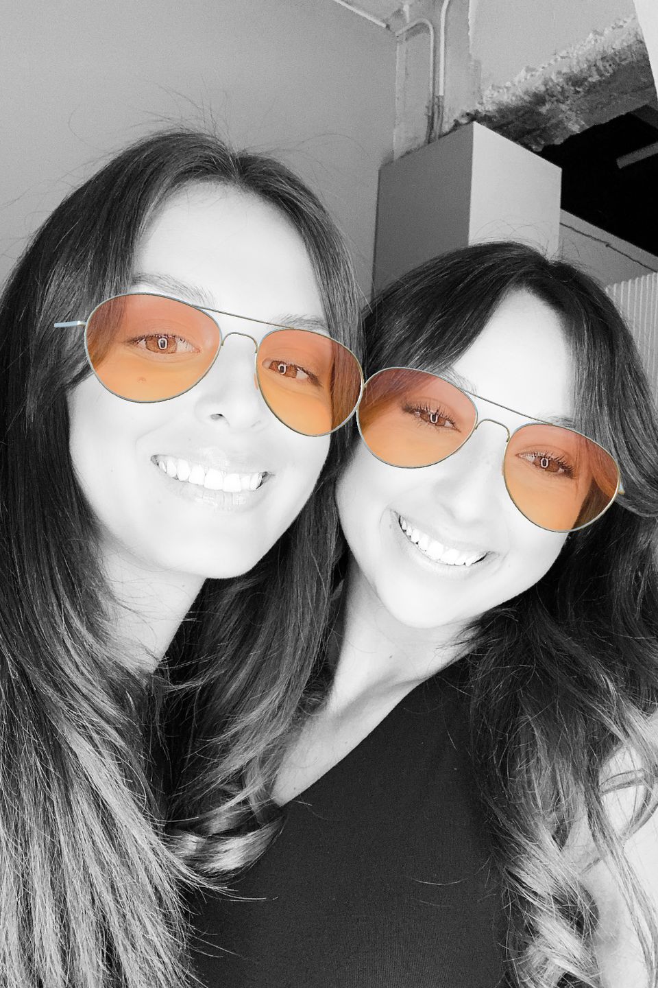Two women smiling while wearing a virtual sunglasses filter in a photo booth.