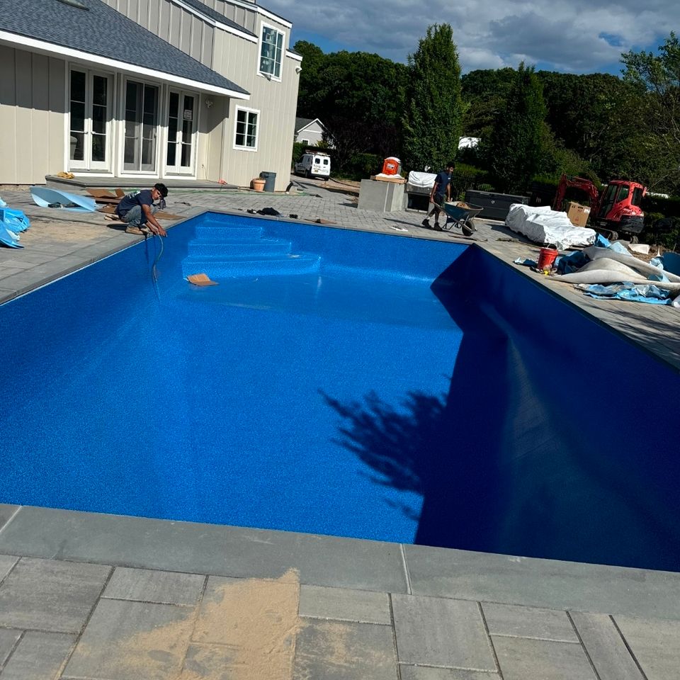 Technician setting a new blue liner in a large rectangular inground pool with bluestone deck in Long Island NY