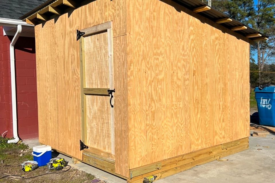 New plywood storage shed with metal roof under construction beside brick building in Virginia Beach VA