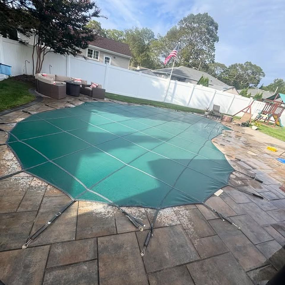 Green mesh safety cover secured over an inground pool on a paver patio in Long Island NY