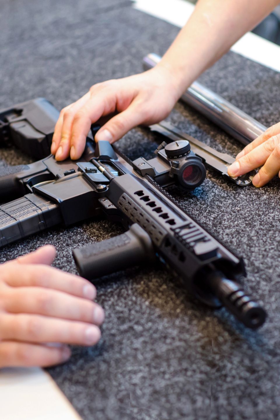 Customer hands examining a rifle with a red dot optic on a gun shop counter