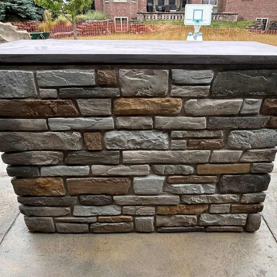 Outdoor stone structure with layered veneer stone surrounding a pool area.