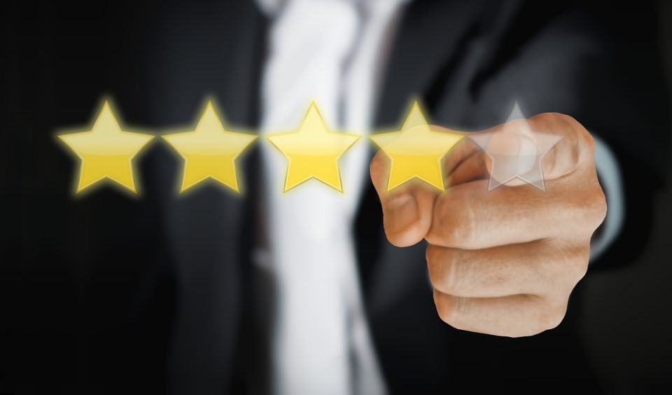 4 stars are light up in front of a person. There is a fifth star that's not lit up. Blurred in the background, a man wearing a suit points at the fifth star