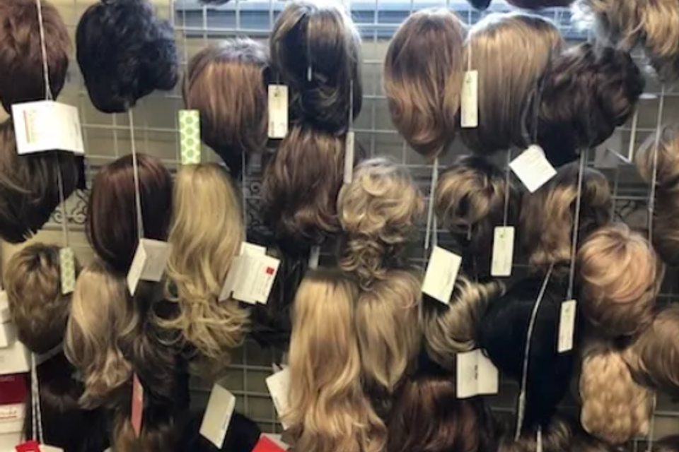 Display of wigs in a variety of colors, lengths, and styles hanging on racks inside Shears Wigs & Hairpieces Salon.