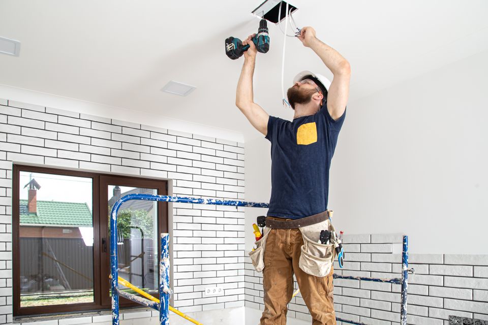 Electrician builder work installation lamps height professional overalls with drill repair site