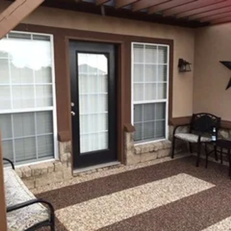Covered patio with decorative stone flooring, striped accent design, outdoor seating, and a bench.