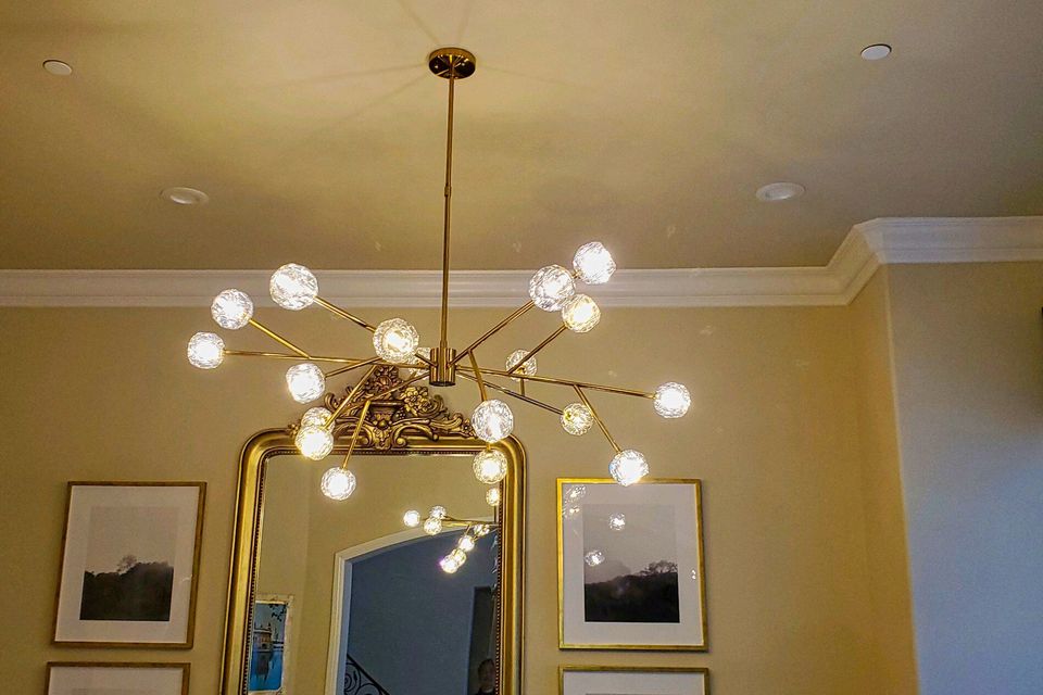 A large, modern gold sputnik-style chandelier with multiple glowing glass globes installed in a luxury living room with high ceilings.