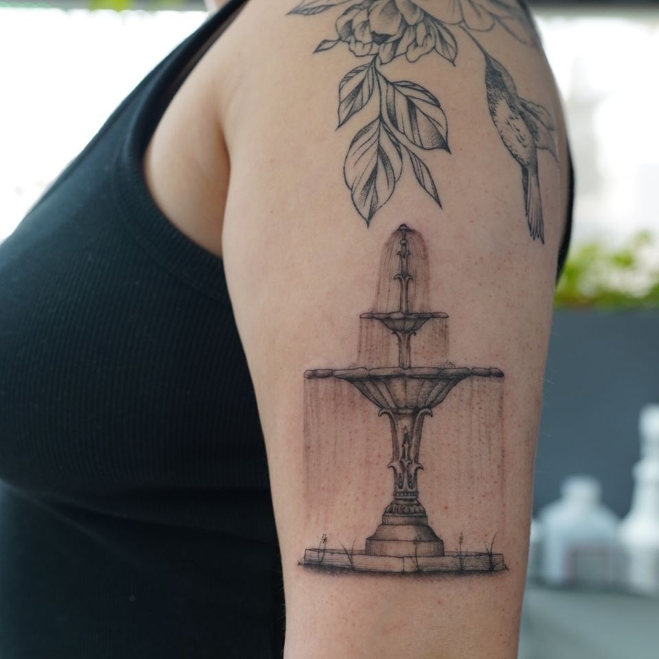 Image of a fountain tattoo in black and grey with detail of water falling down each level of the 3 level fountain