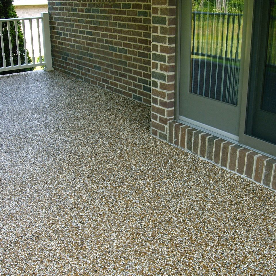 Covered porch with stone epoxy flooring beside a brick exterior and white railing.