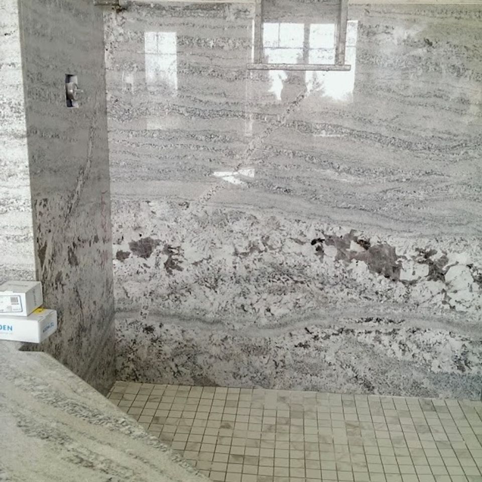 Luxury walk-in shower featuring large-format Granite slab walls with heavy veining, a custom soap niche, and mosaic floor tile—Master bathroom stone masonry by LuXe Design.