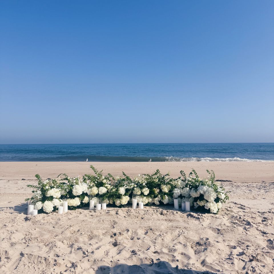 Low hydrangea and greenery ceremony installation with pillar candles set on a Hamptons NY beach