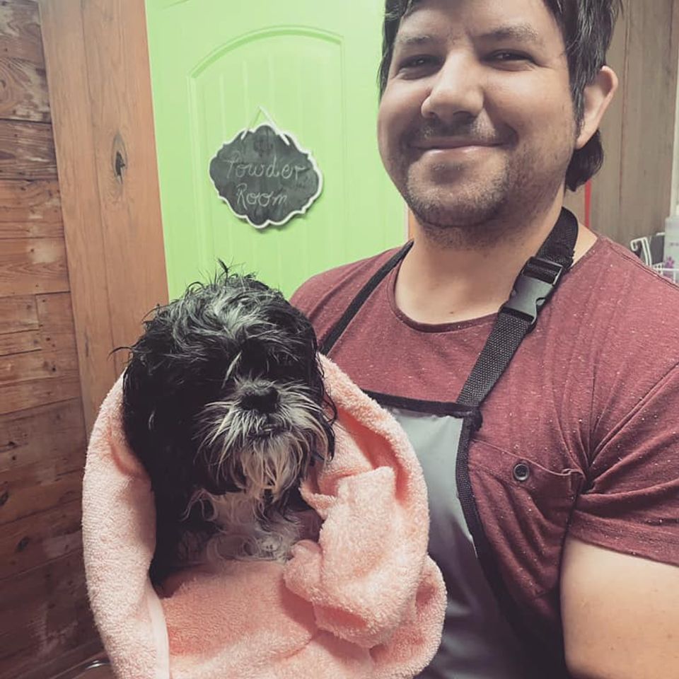 Small black dog wrapped in towel after bathing   with dog groomer