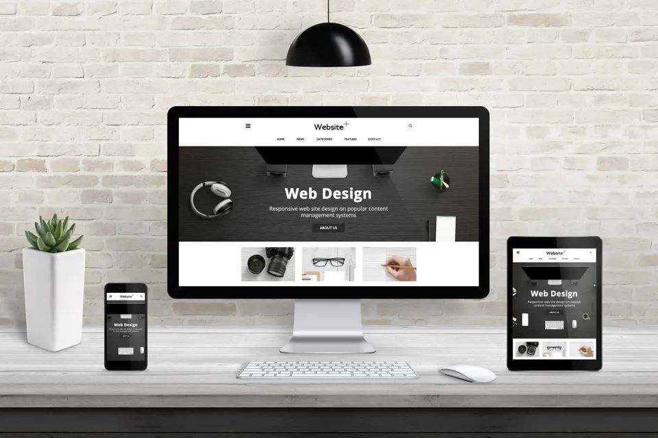 Website being designed and displayed on a desktop, tablet and mobile phone screen. White room.