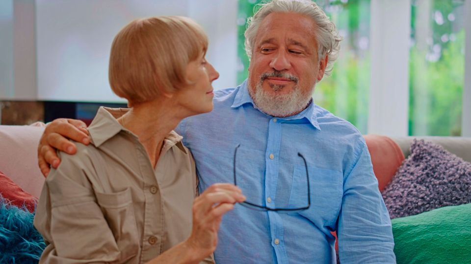 Senior woman taking off eyeglasses from man mature couple sitting on couch at home por sbi 351282430