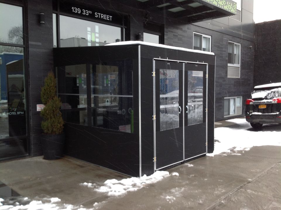 Black framed seasonal vestibule with double glass doors at a New York City building entrance, snow on the sidewalk