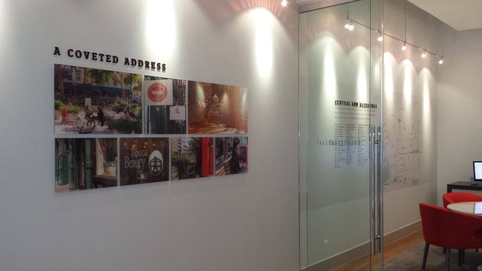 Interior display for The Leonard, dimensional letters reading A Coveted Address above a grid of printed photo panels, beside a frosted glass wall with a printed neighborhood directory