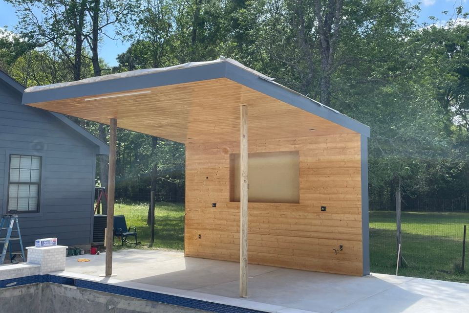 Finished custom steel poolside cabana with wood accents and covered outdoor gathering area in Houston.