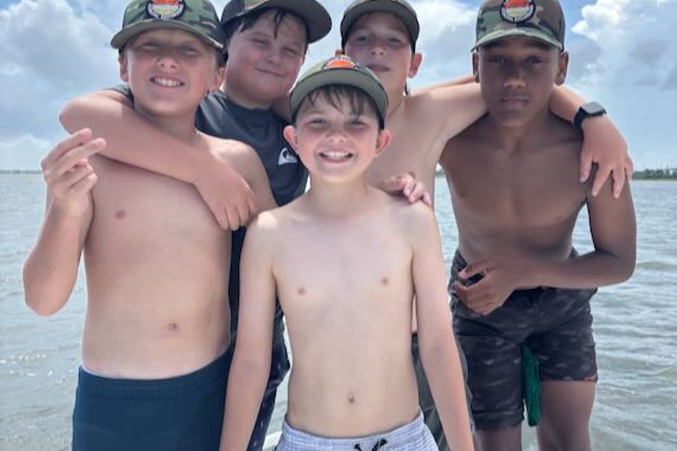 Group of smiling kids on a Charleston boat camp with LowCountry Coastal Excursions, wearing matching hats and enjoying a sunny day on the water