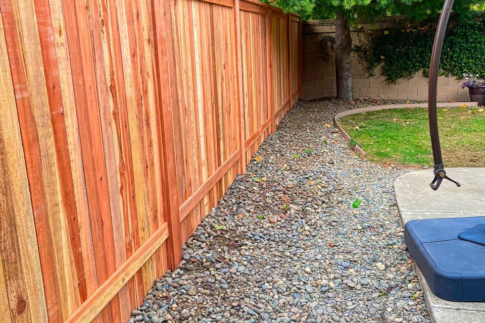Freshly built wooden fence beside curved river rock landscaping and concrete patio