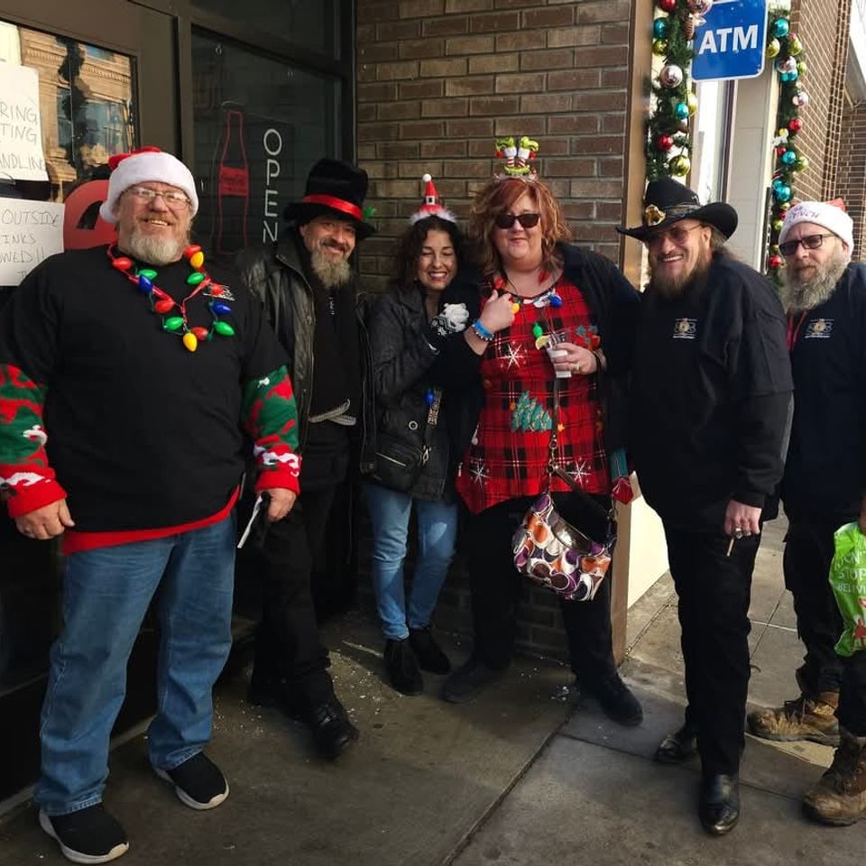 Group of event attendees wearing Christmas-themed outfits and accessories while posing on a downtown sidewalk.