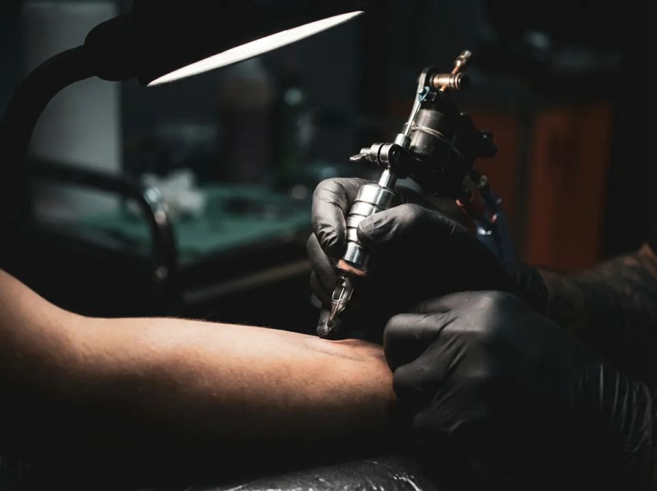 Close-up of professional tattoo artist wearing black gloves using a machine to tattoo a client's forearm