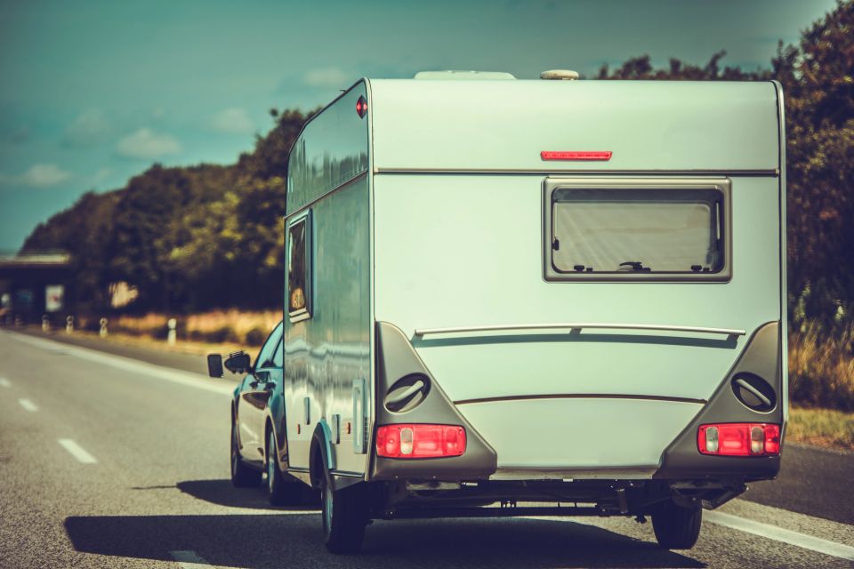Rear view of a white camper trailer towed down a sunny highway representing travel trailer title loans