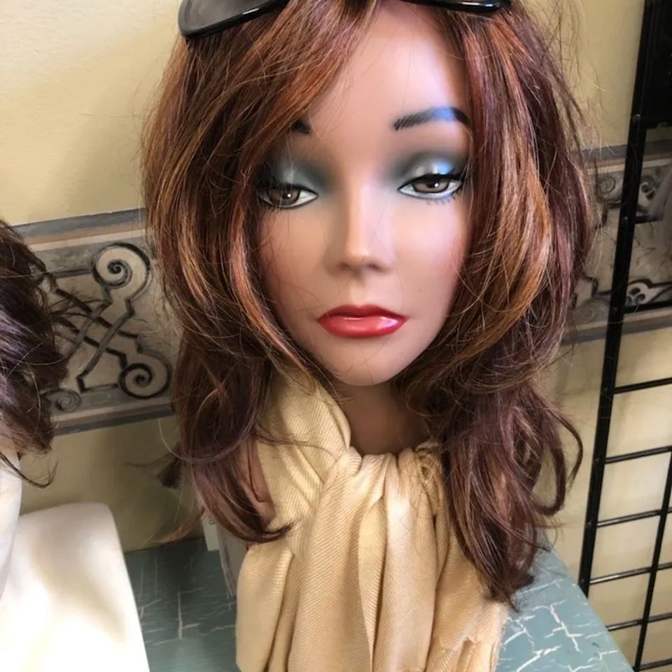 Medium-length auburn wig with soft layers and side-swept bangs displayed on a mannequin wearing a light scarf and sunglasses at Shears Wigs & Hairpieces Salon.