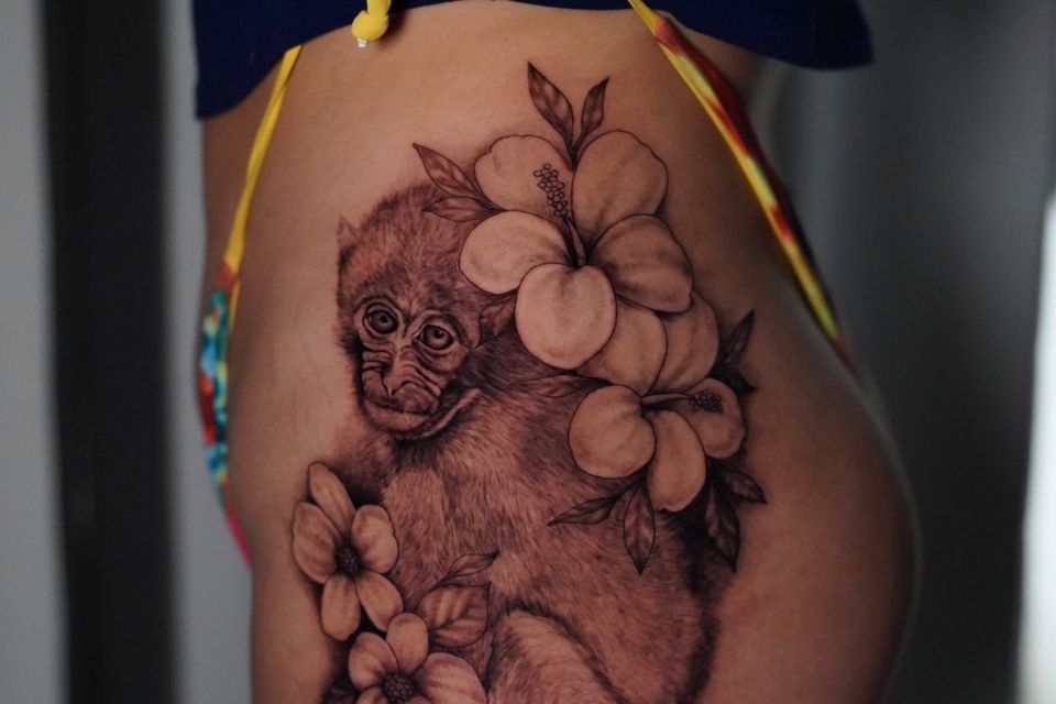 Image of a woman's thigh with a black and grey tattoo of a Monkey with white flowers all around