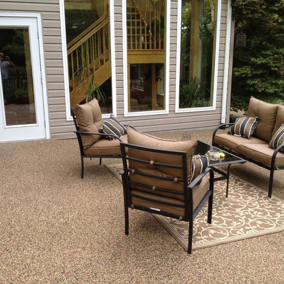 Decorative stone patio with outdoor furniture outside a home featuring large windows and patio doors.