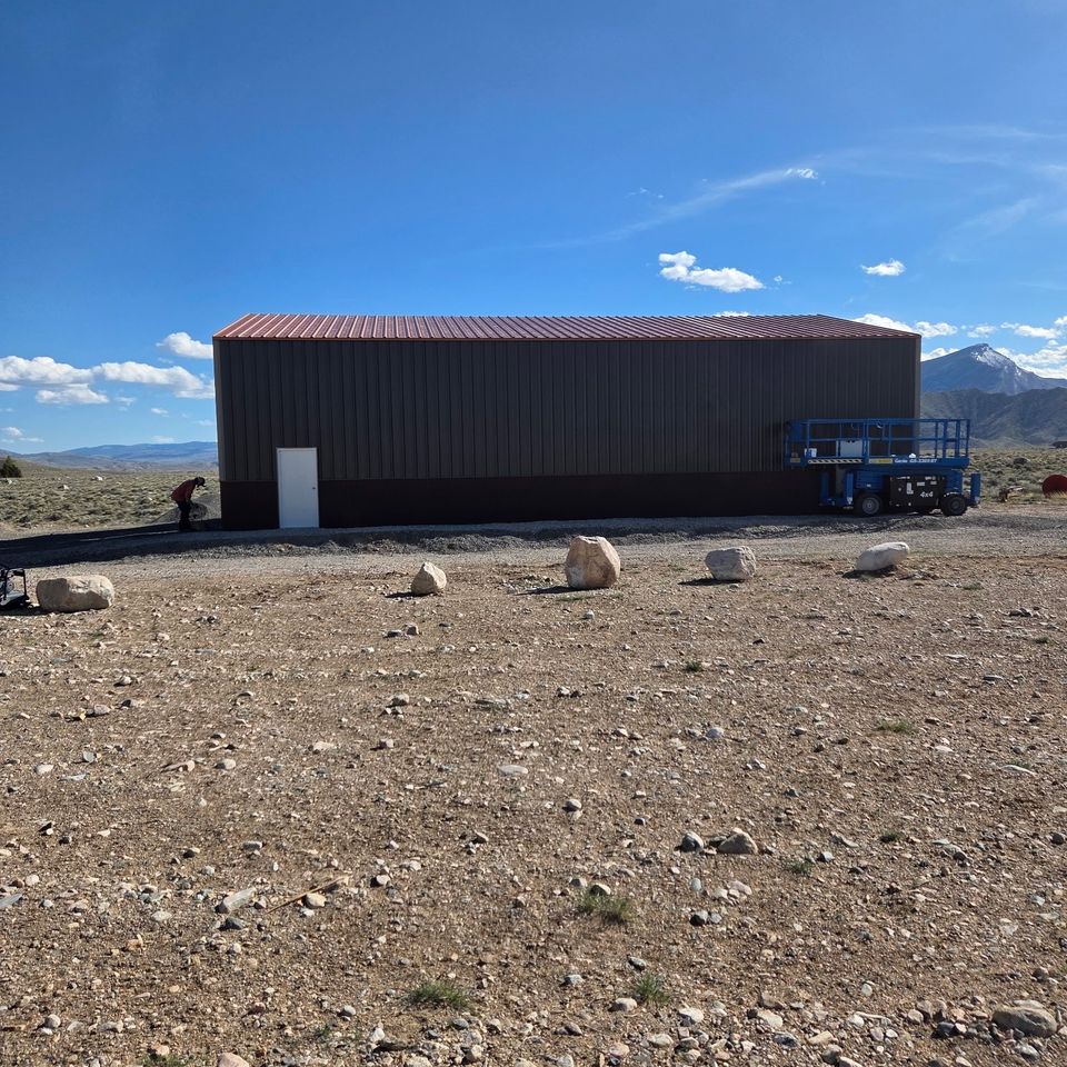 Completed dark brown metal building with red roof on open lot in Trout Creek MT