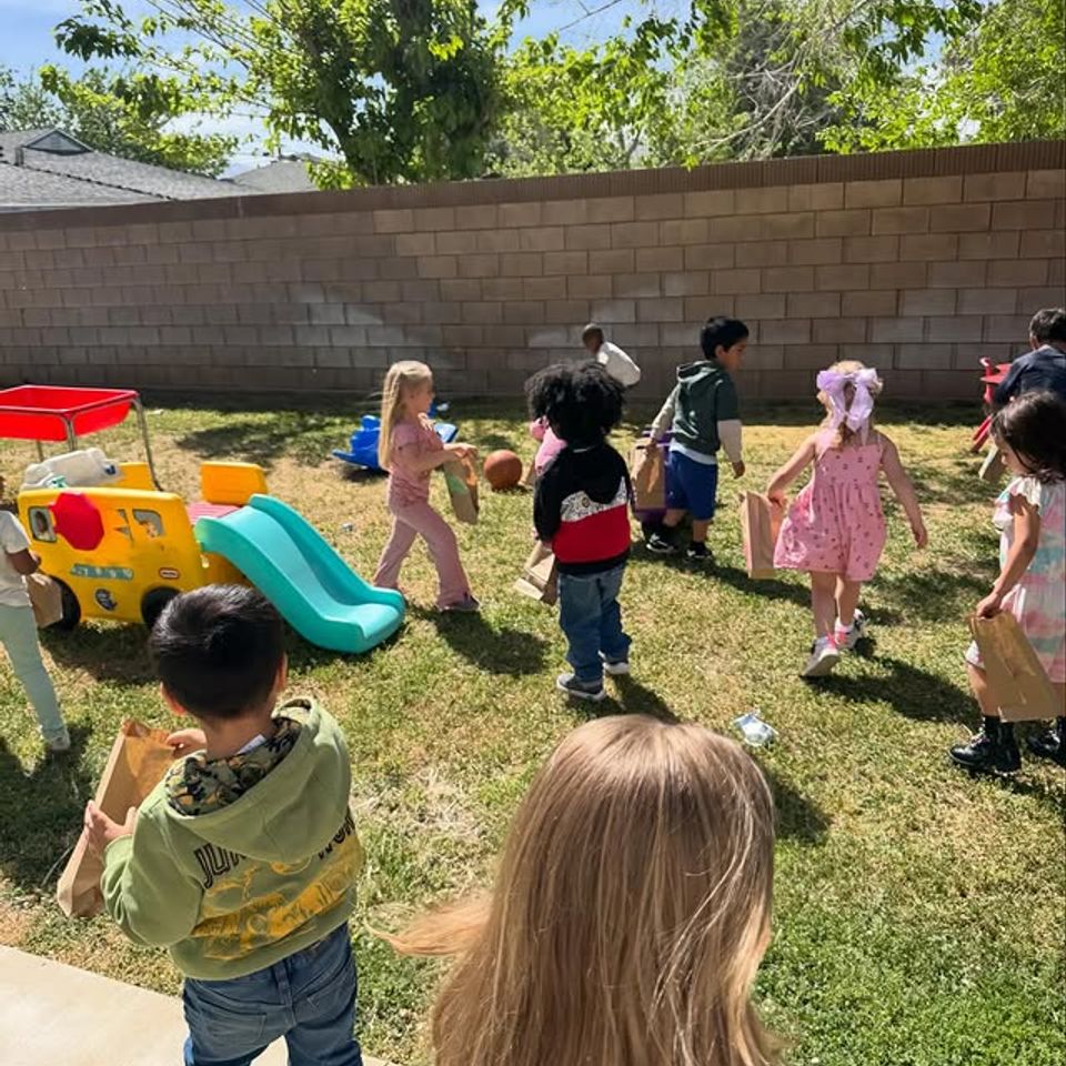Preschool children carrying paper bags during an outdoor egg hunt in the daycare backyard in Palmdale CA