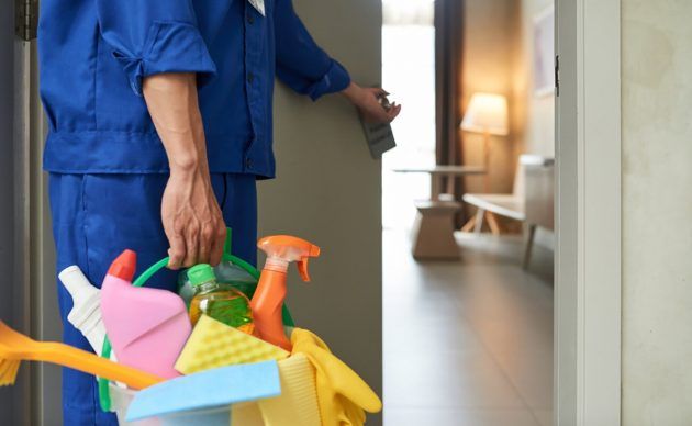 Unrecognizable cleaner walking into hotel room with tools detergents 630x388