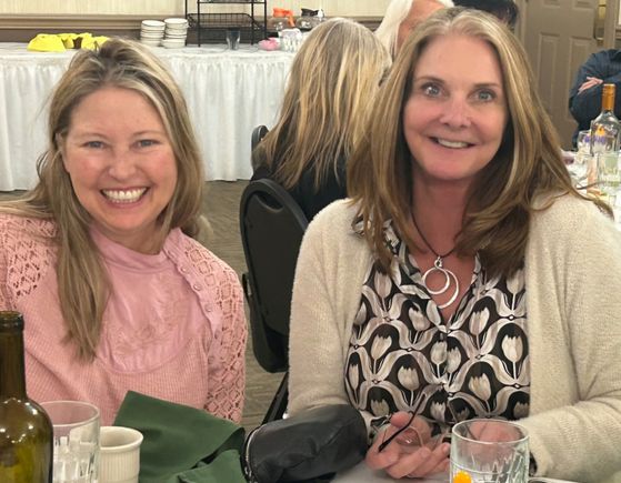 Two women smiling for a photo while seated at a luncheon table.