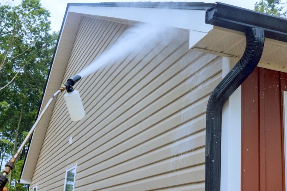 A person spraying the exterior of a house cleaning it