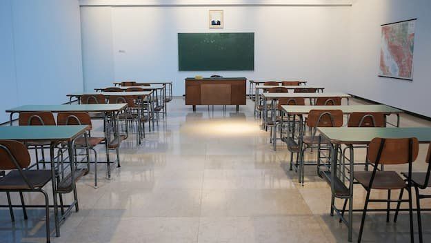 A classroom with desks and a green "blackboard" at the front of the room 