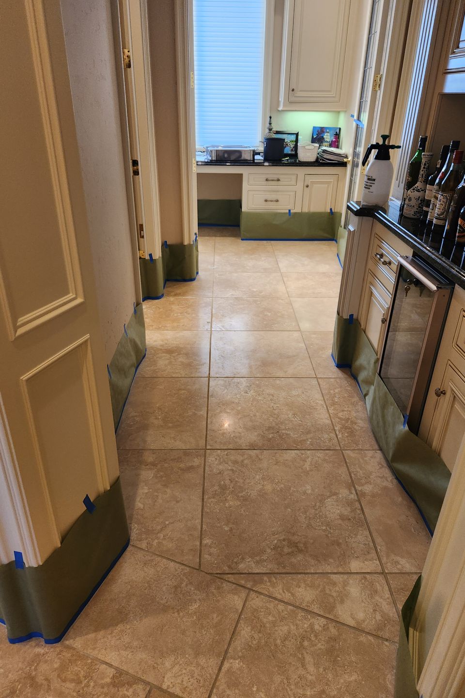 Kitchen with beige tile floor and cream cabinets covered in green protective paper and blue tape during renovation or maintenance work