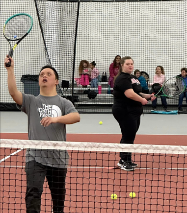 Participant with Down syndrome practicing tennis skills on an indoor court during an adaptive sports program.
