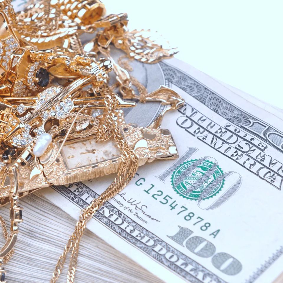 Pile of gold jewelry on top of one hundred dollar bill