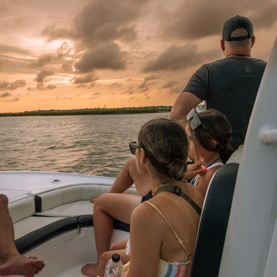 Passengers relaxing on a Charleston sunset boat cruise, watching the colorful evening sky over the water